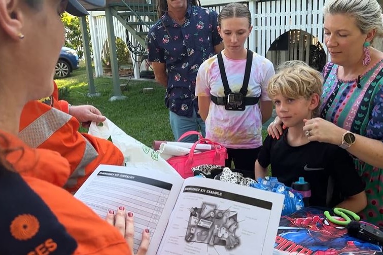 An SES worker with an emergency action guide, standing near a table with a young family