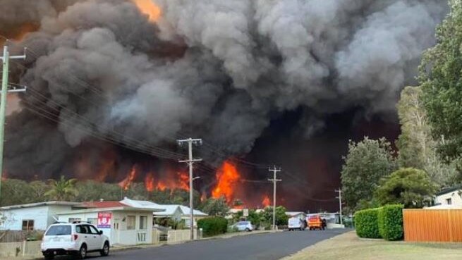 Red flames and thick black smoke can be seen immediately behind houses.