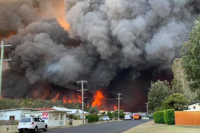 Red flames and thick black smoke can be seen immediately behind houses.