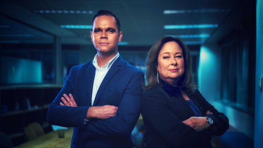 Allan Clarke and Suzie Smith with arms crossed looking to camera in office with blue light in background.