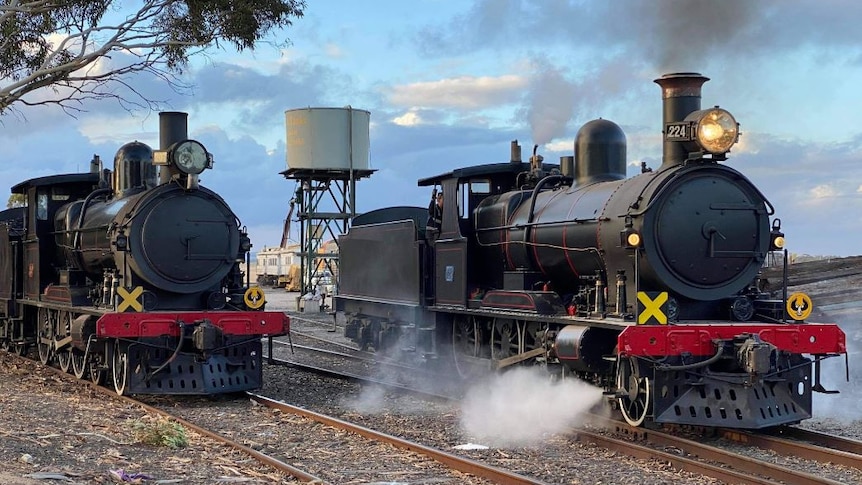Two black steam trains side by side on train tracks 