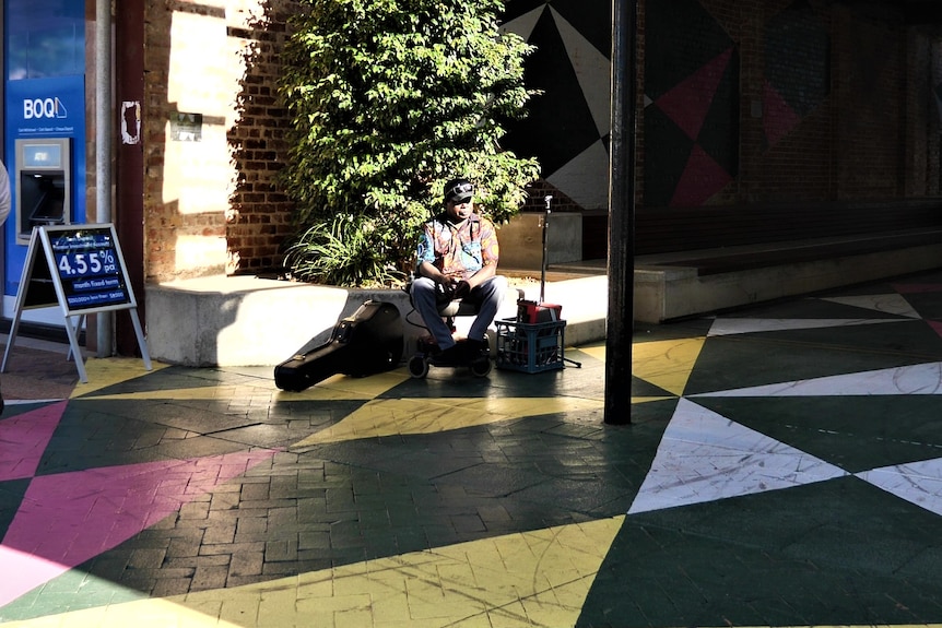 Man sitting in the sun in town with bright patterned floor.