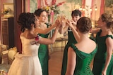 Alisha Boe (left) wears a white 1870s wedding dress as she cheerses to four other women in emerald gowns.