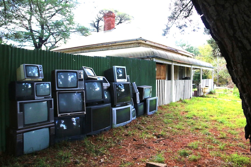 Old television sets propped up against green fence