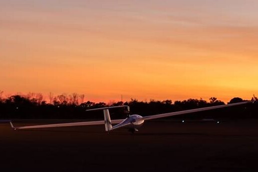 A glider on the ground at an airport on sunrise.