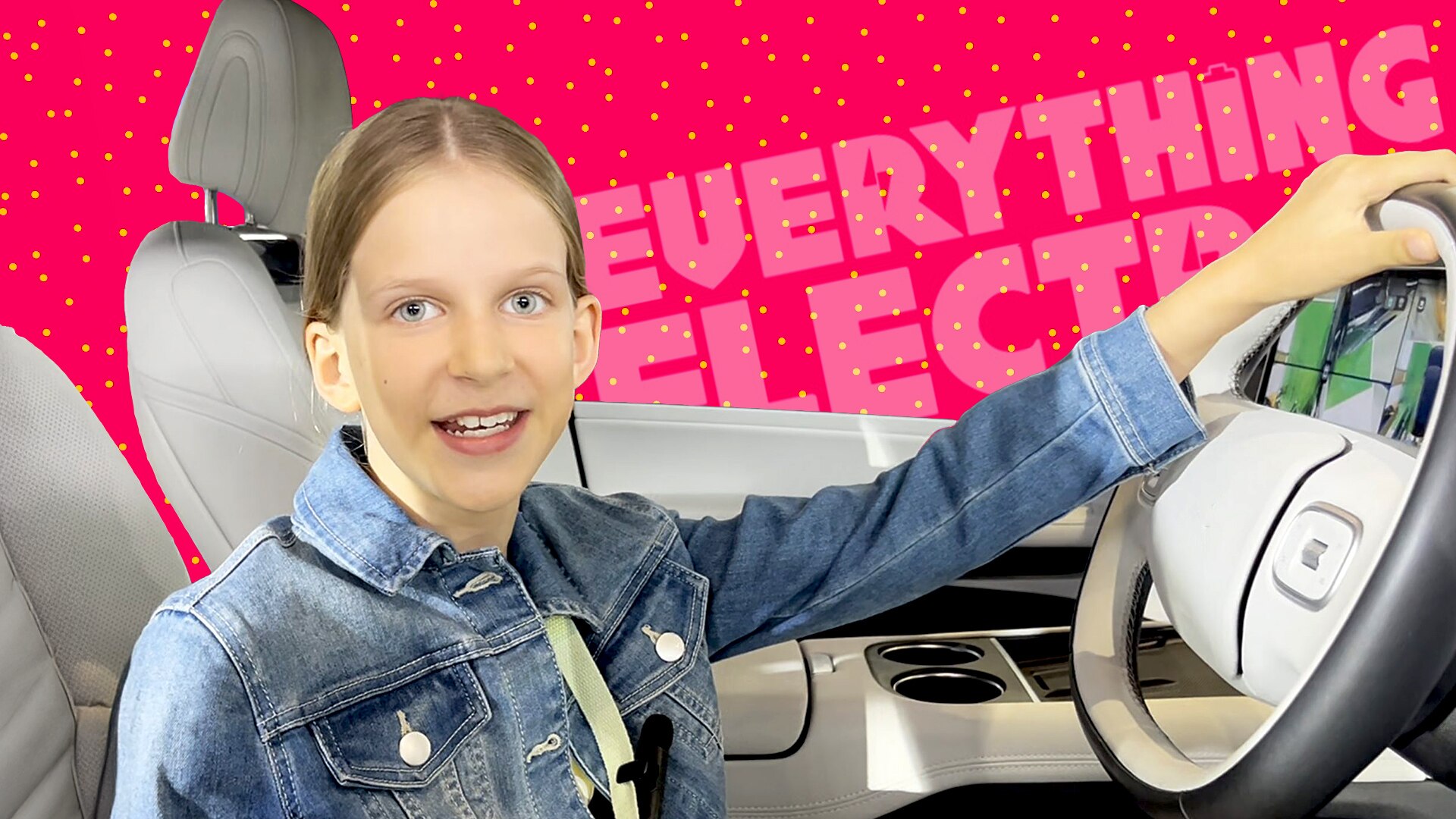 Hannah smiles while she sits in an electric car holding the steering wheel.