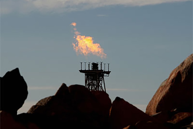 A gas flare at Woodside's North West Shelf Venture in Western Australia, with rocks in the foreground.