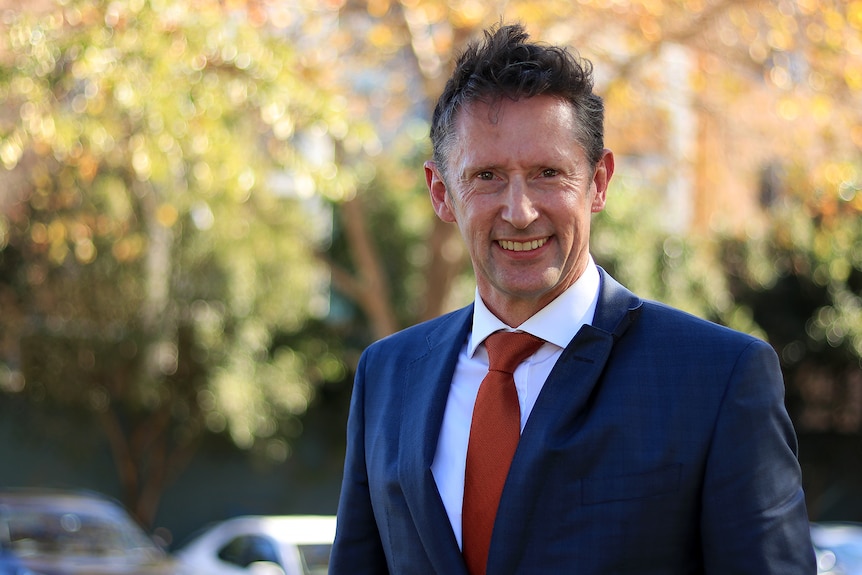 A man in a suit with red tie smiles