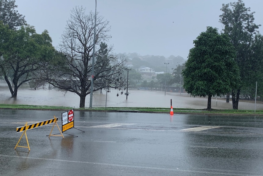 Signs showing road closed by floodwaters in Gympie, flooded oval in the background
