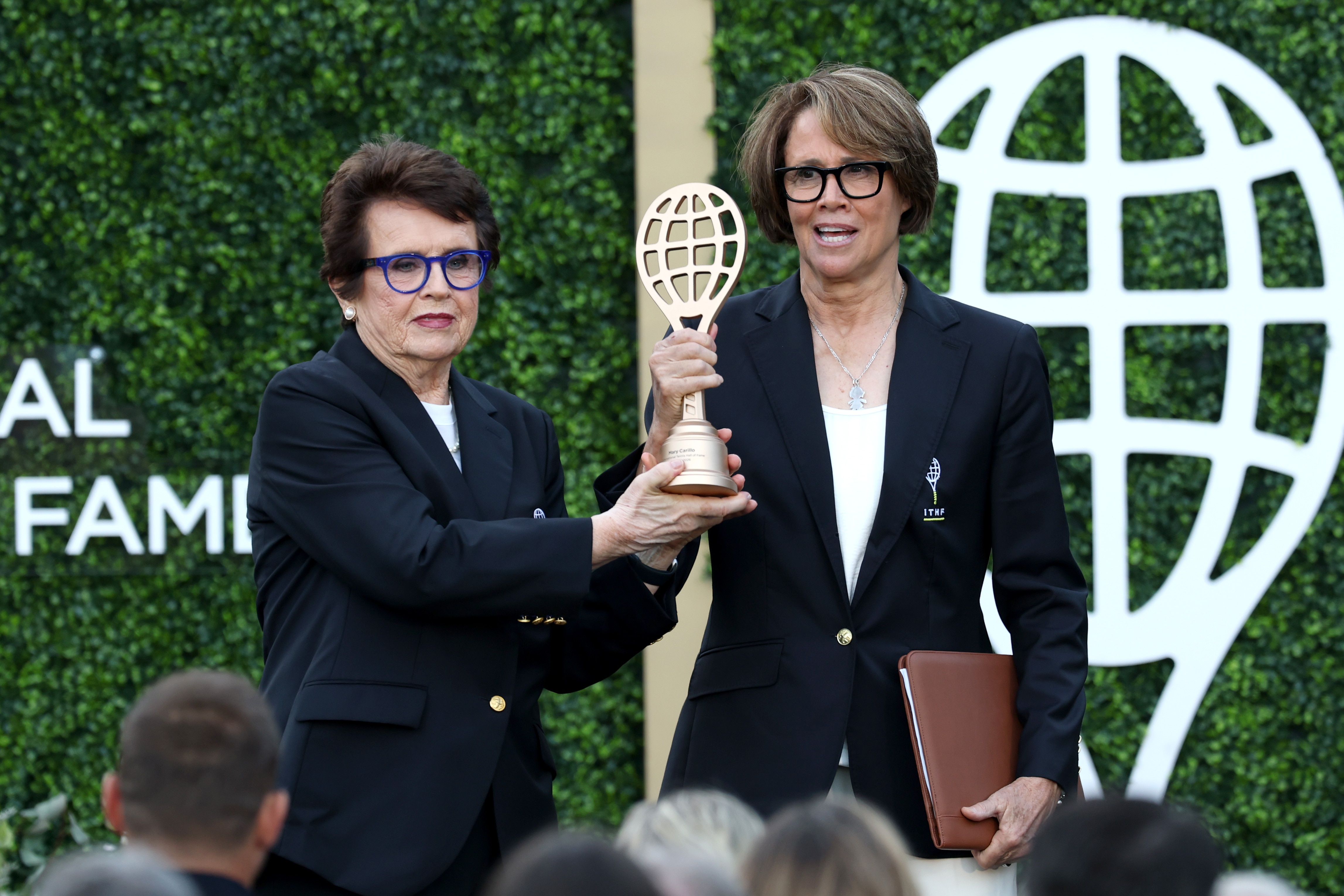 Tennis great Billie Jean King (left) stands next to broadcaster Mary Carillo (right) holding a trophy at a Tennis Hall of Fame