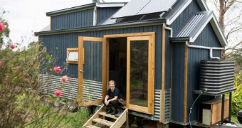 A woman sits on the steps of her tiny house in country Victoria.