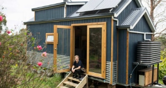 A woman sits on the steps of her tiny house in country Victoria.