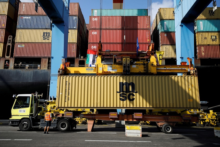 A truck carrying a shipping containers waits to be unloaded at a container terminal