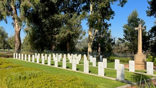 Image shows green lawns, rows of white headstones and a large stone cross