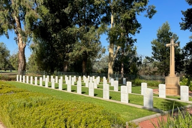 Image shows green lawns, rows of white headstones and a large stone cross