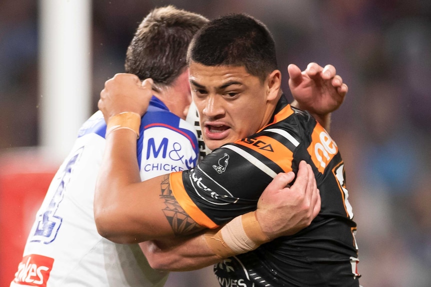 A Wests Tigers NRL player is held in a tackle made by a Canterbury opponent.