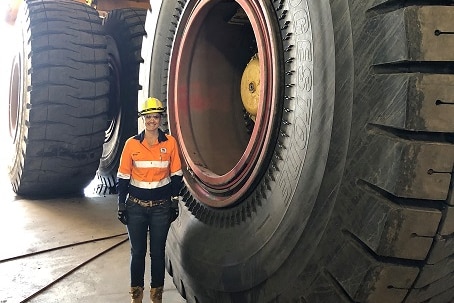 A woman wearing a hard hat and a high viz shirt stands in front of a very big wheel