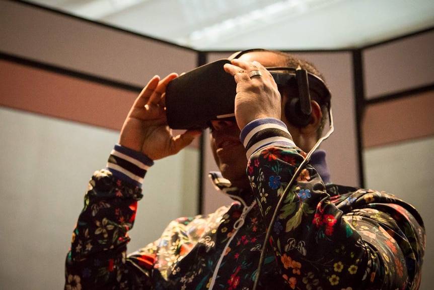 A man is smiling as he wears a set of virtual reality goggles at the National Gallery of Australia