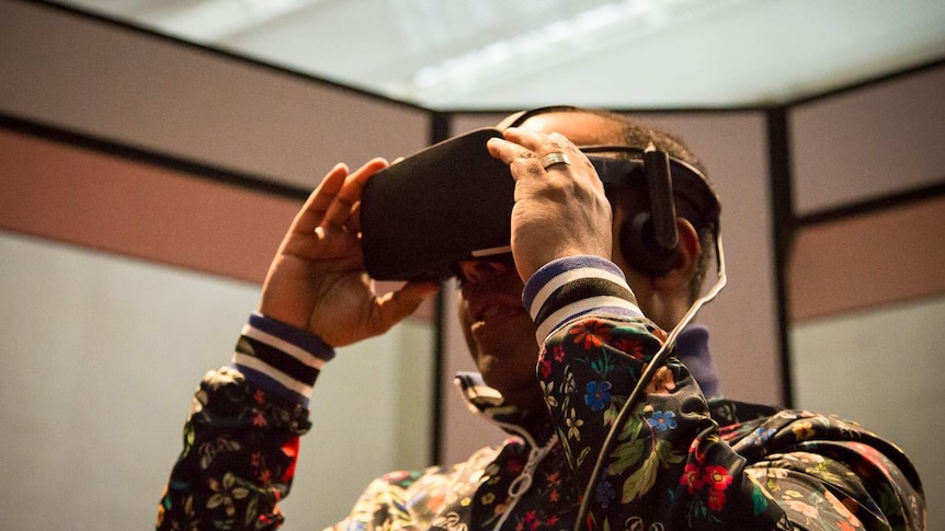 A man is smiling as he wears a set of virtual reality goggles at the National Gallery of Australia