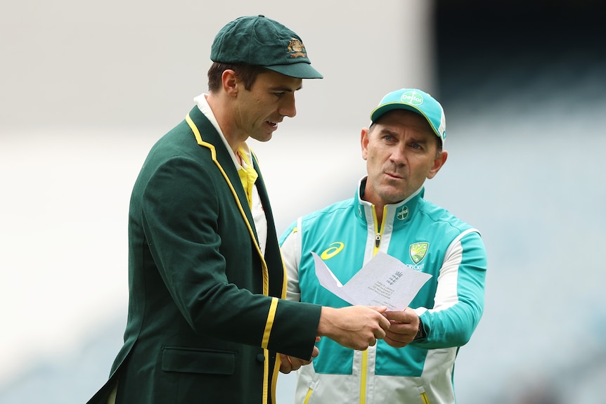 An Australian cricket coach stands with his captain looking at a piece of paper. 