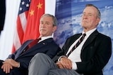 George W Bush and his father George HW Bush look concerned as they sit in front of an American flag.