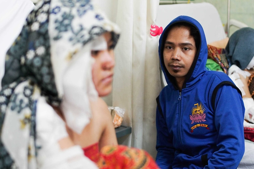 A man sits beside his wife's bedside in a hospital