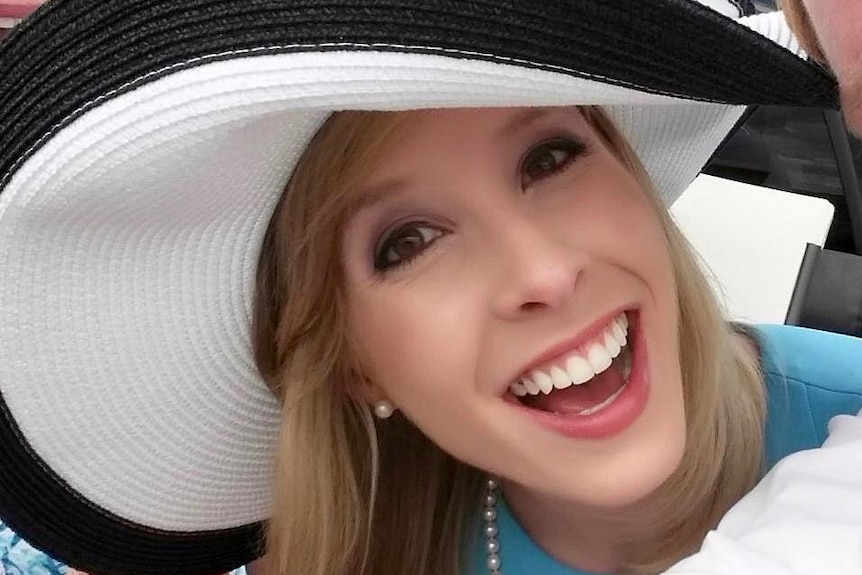 A young blonde woman smiling in a big hat