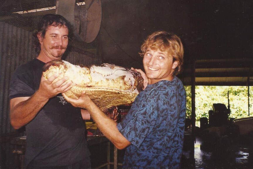Two men both holding up a severed crocodile head 