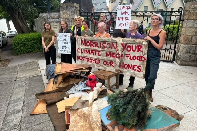 Women standing holding protest signs with rubbish infront of them