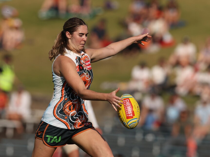 A GWS AFLW player drops the ball onto her boot to kick for goal during a match.