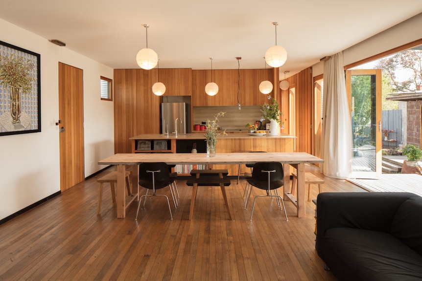 An internal shot of the lounge room and kitchen featuring wooden floorboards, wall linings and joinery.