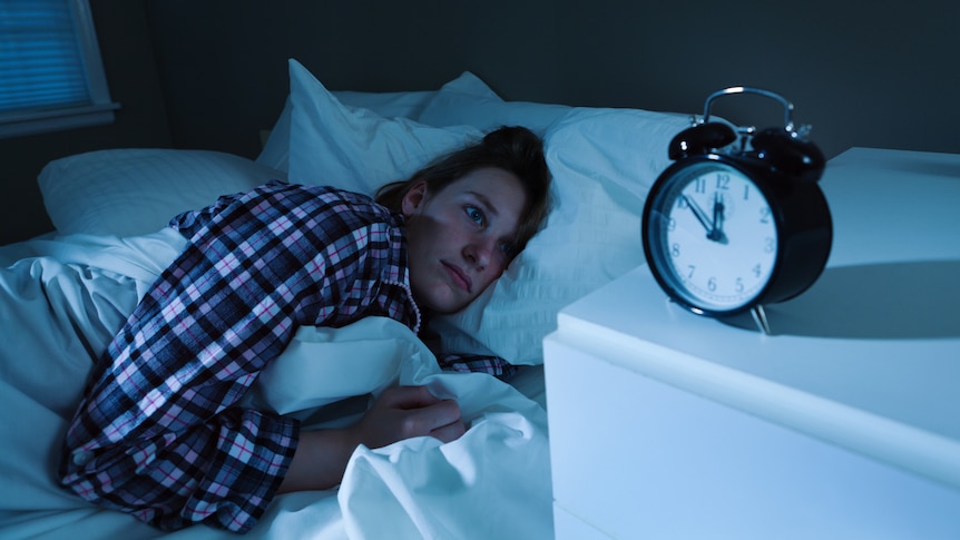 A woman laying in bed late at night awake, watching the clock and worrying