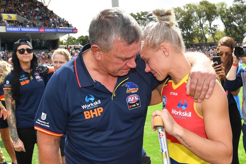 A man comforts his daughter who is holding on to a crutch.