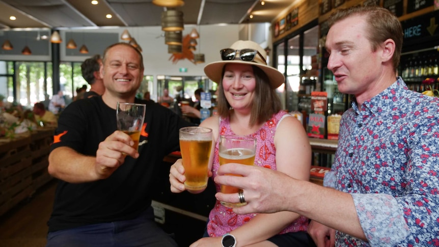 Three people holding beer in brewery.