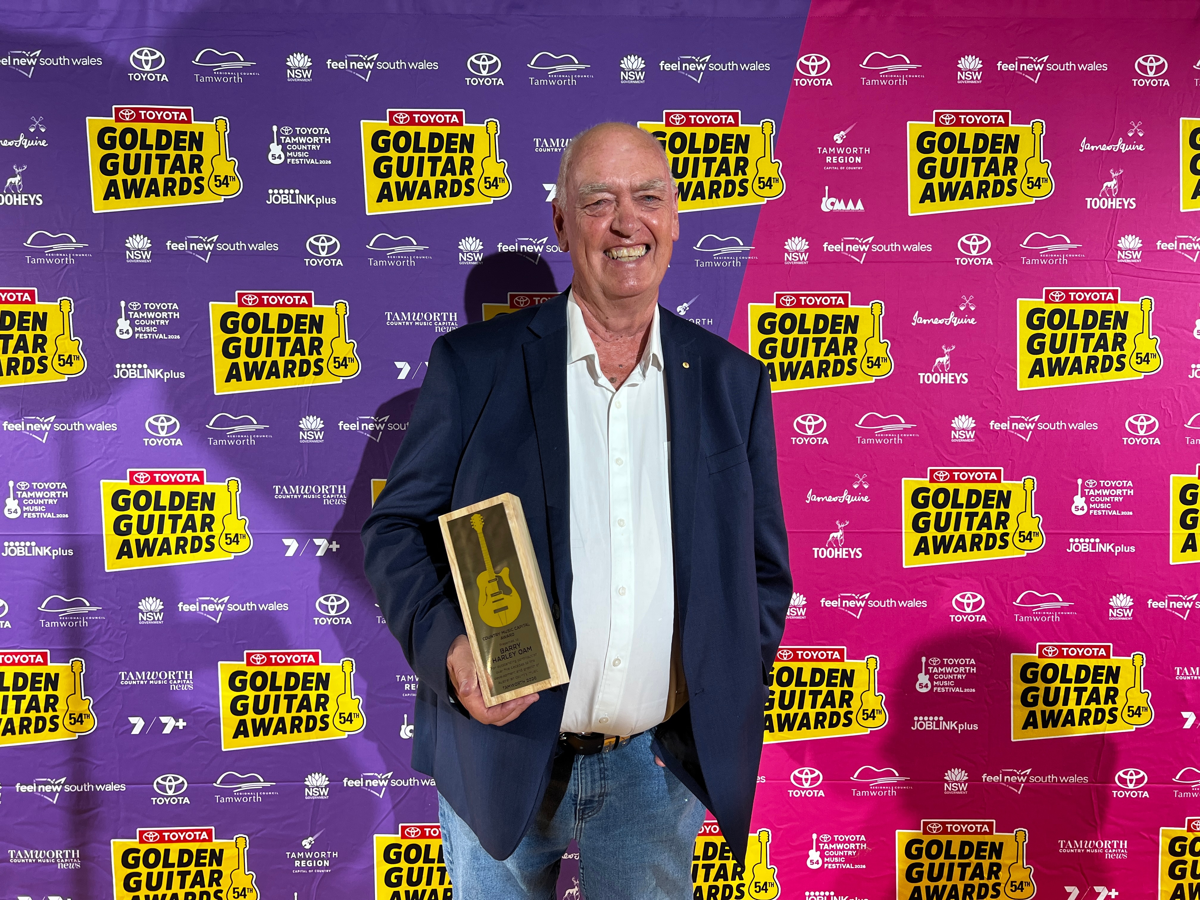 Um homem de terno sorri e segura um prêmio.