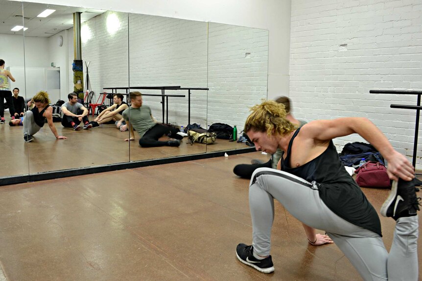 A man stretches in a dance studio in front of the mirrors.