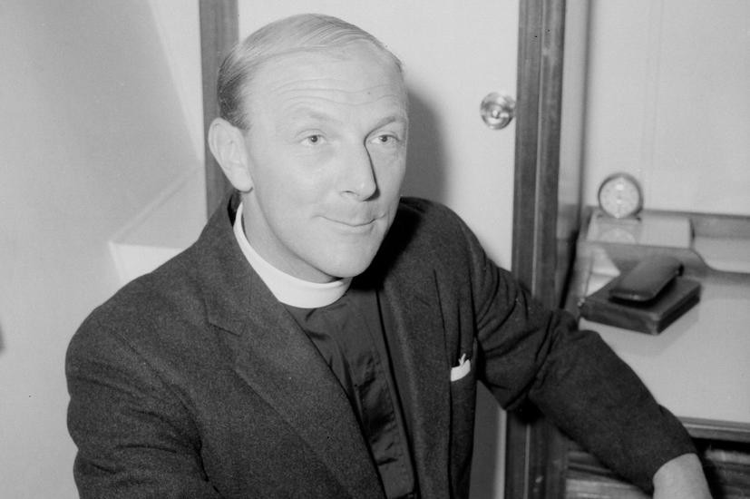 An old photo of a priest smiling for a photo.