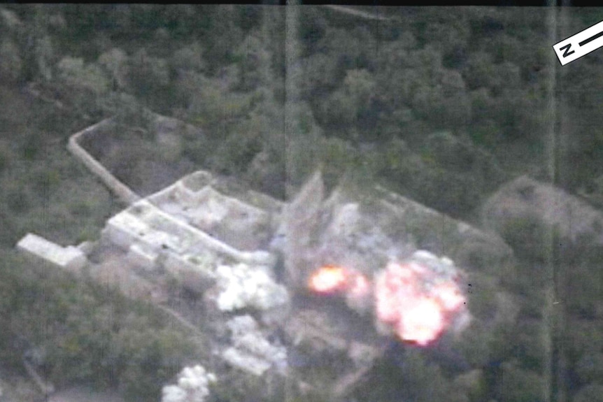 A grainy image of a building seen from above that has been hit by explosives. 