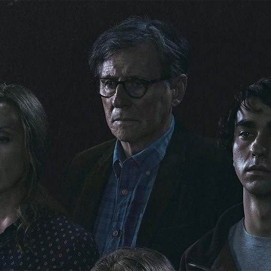 Three people standing in front of a black backdrop. A father in the middle wearing glasses, a young girl with