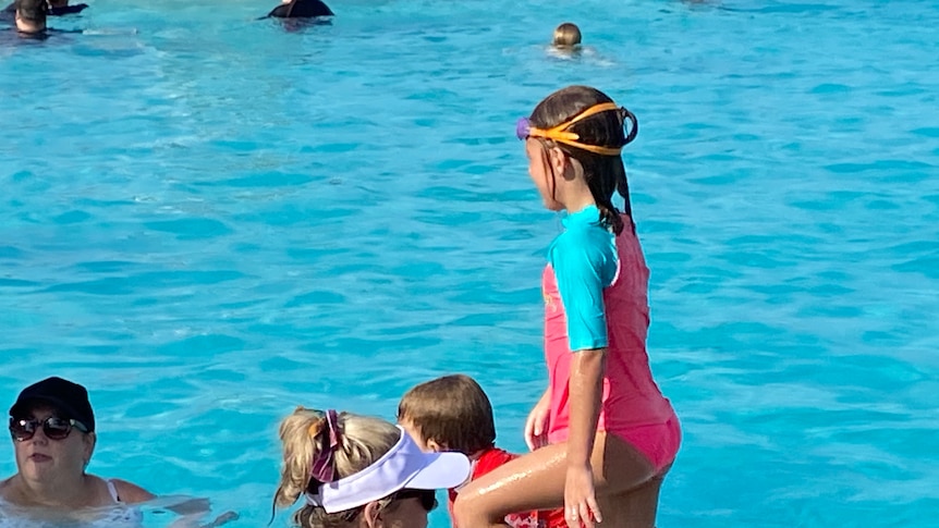 A young girl in swimmers in a pool with other people around