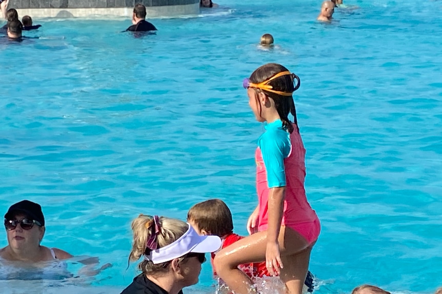 A young girl in swimmers in a pool with other people around