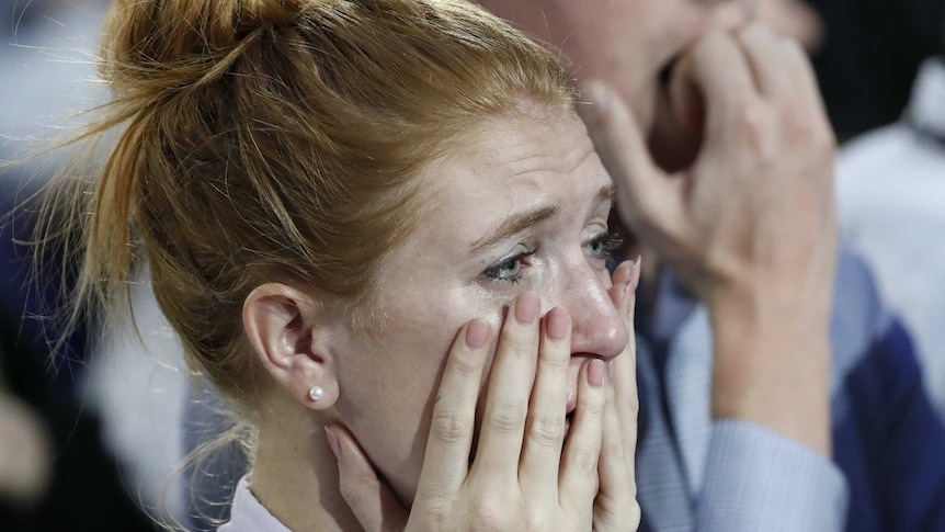 An emotional Hillary Clinton supporter holds her hands to her face.