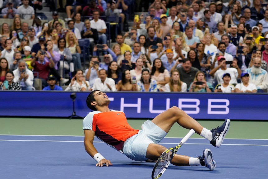 Spain's Carlos Alcaraz falls on the court, as he drops his racquet in reaction to winning a grand slam singles title.