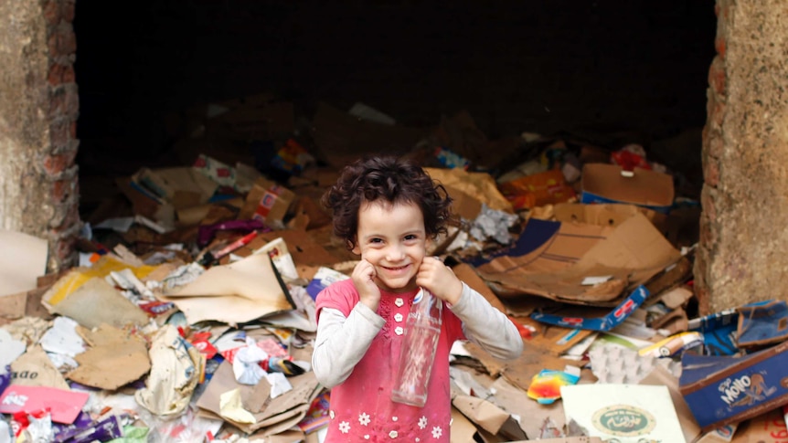 A young girl smiles as she stands among rubbish at a garbage dump in Cairo.