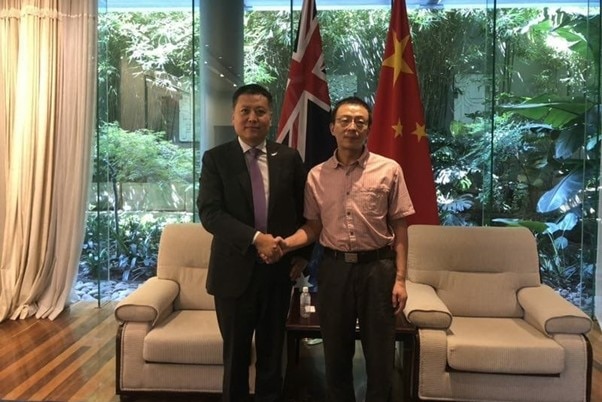 Chinese men shake hands in front of flags of Australia and China.