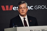 Medium close up of Westpac chief executive Brian Hartzer wearing a black suit, seated in front of a sign reading Westpac Group