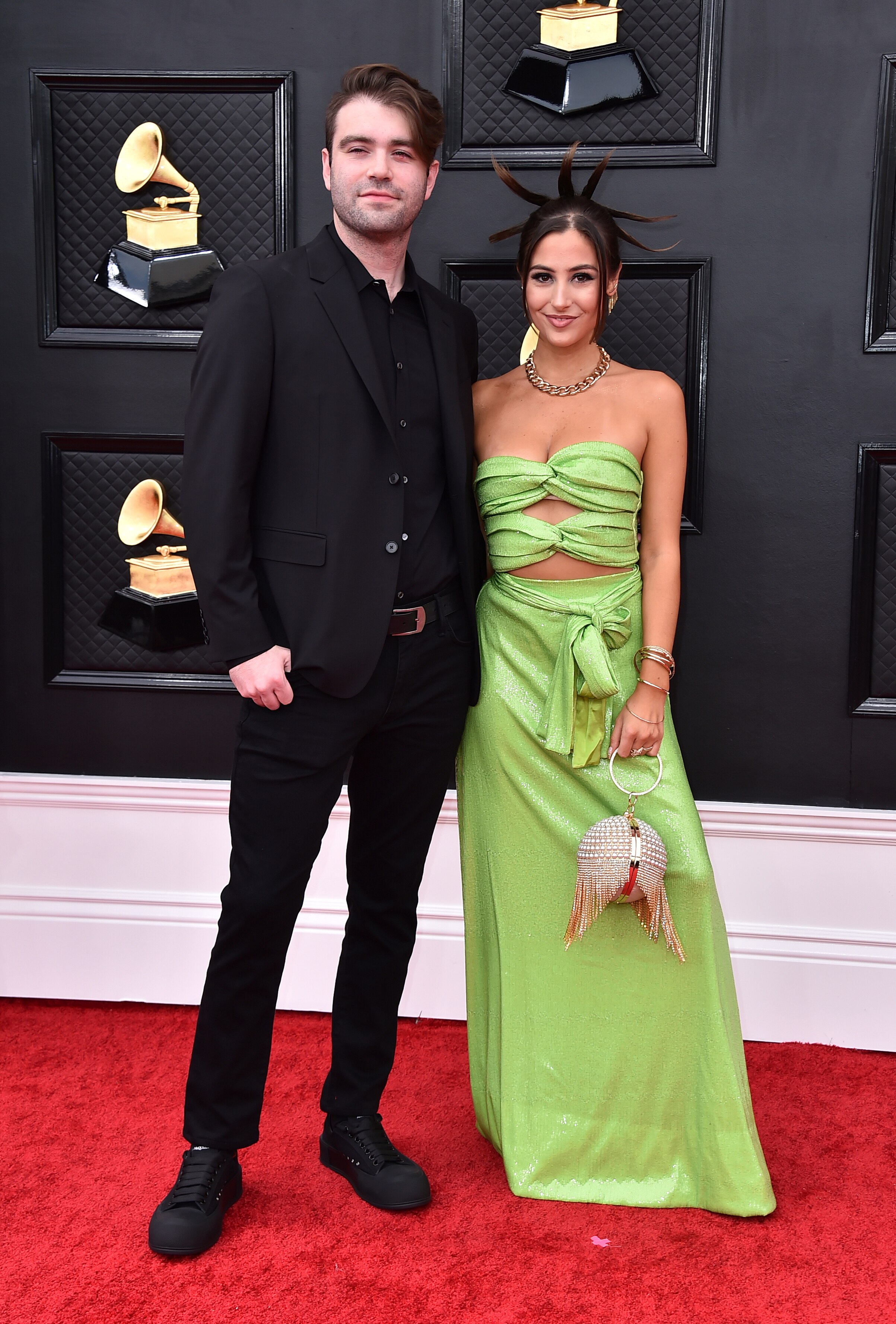 Jake Torrey and Tia Tia stand arm in arm on the grammy red carpet. Tia Tia has her hair spiked up in six spikes 