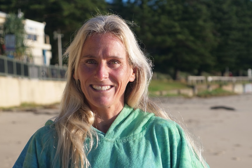 Blonde woman wears hooded beach towel and smiles at the camera 