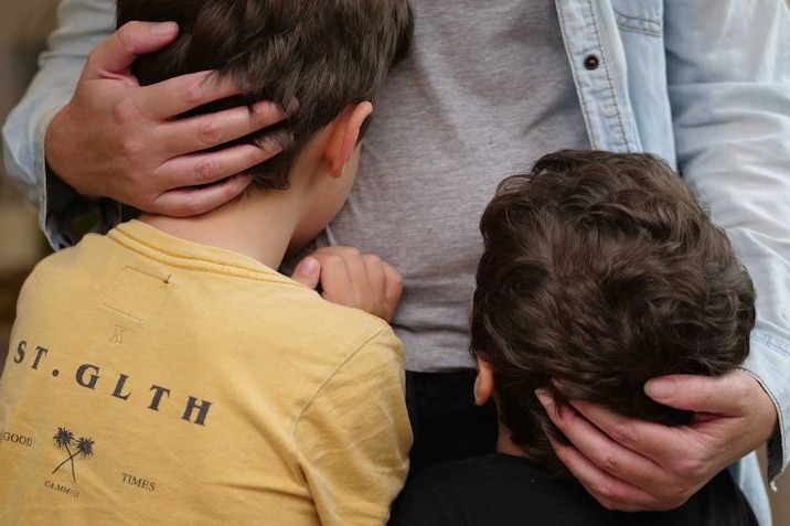 Two kids hug a family member - anonymous. 