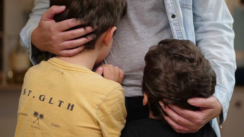 Two kids hug a family member - anonymous. 